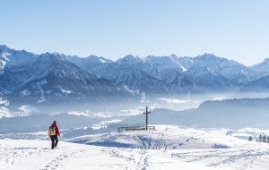 Winterwanderer direkt am Gipfelkreuz vor Bergkulisse am Ofterschwanger Horn©Allgäu GmbH, travelita.ch